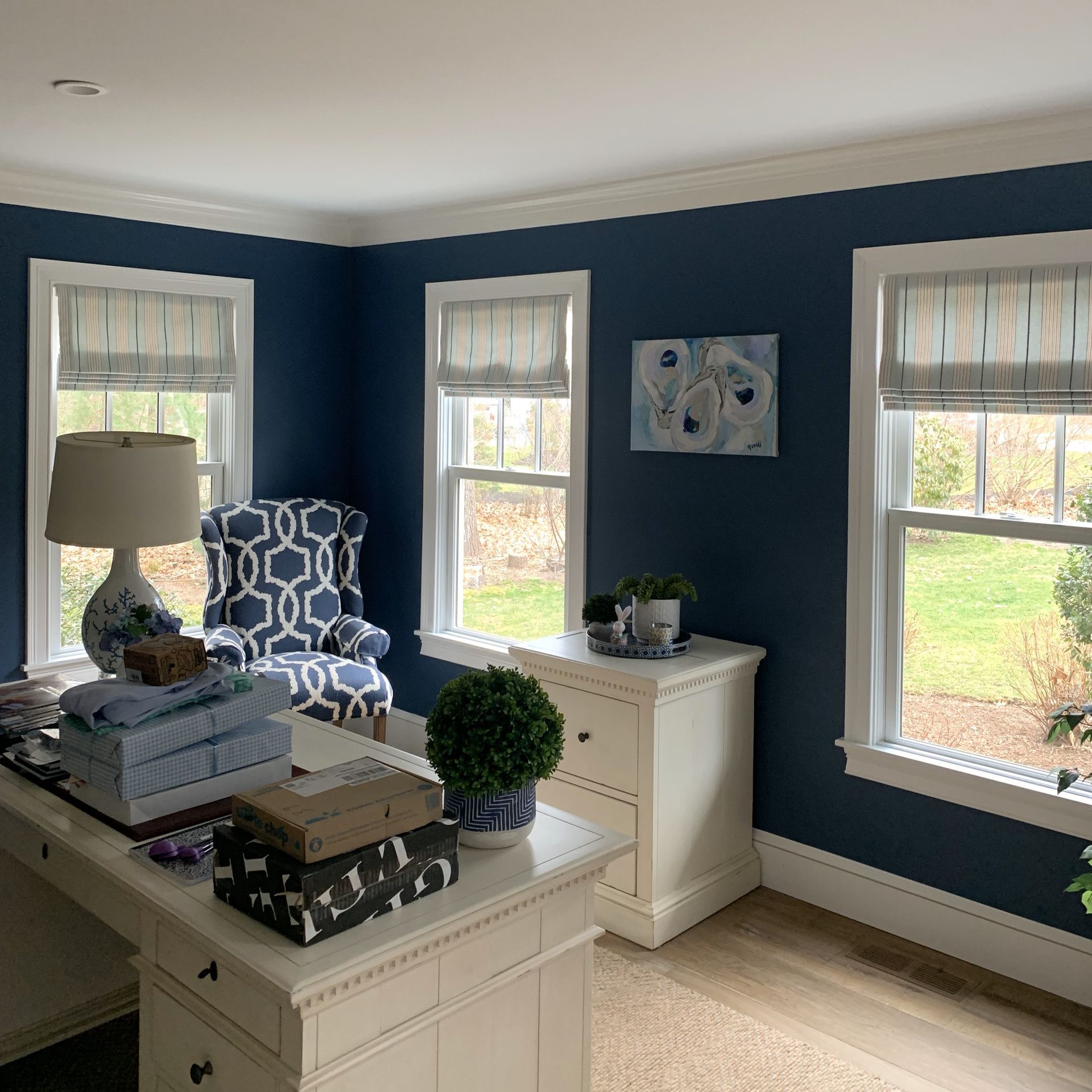 Blue home office with desk, chair, windows, white dresser, and nautical decor