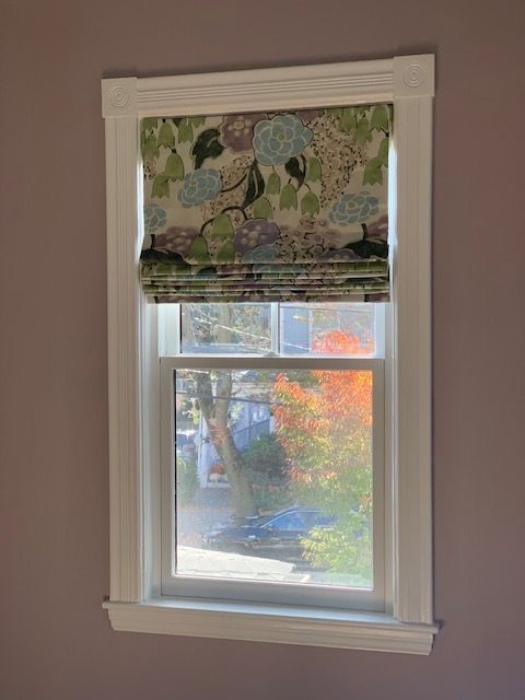 Window with floral Roman shade, white trim, and a view of a tree and parked car outside.