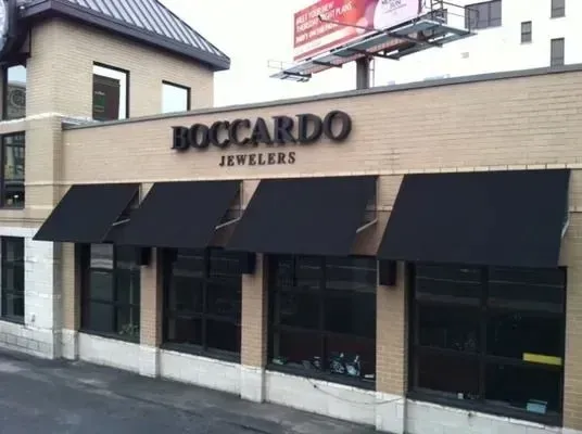 A tan brick storefront for Boccardo Jewelers with four black awnings over large windows.