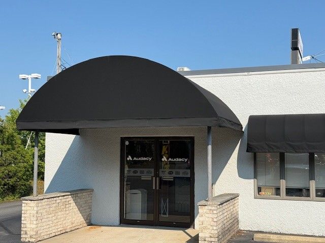 Entrance of a white building featuring a large, black arched fabric awning over double glass doors and a side window.