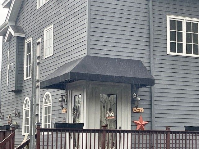 Gray house with a dark blue awning over the front entrance, a wooden railing in the foreground, and a red star decoration.