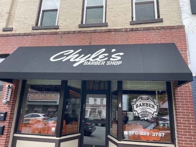 Chyle’s Barber Shop storefront with a black awning and brick facade, showing the business name and phone number on windows.