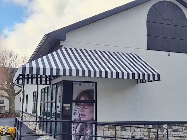 A storefront with a black-and-white striped awning and a large poster of a person wearing glasses in the window.