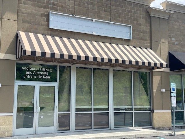 A storefront with a beige-and-brown striped awning and a blank sign above, featuring a sign about rear parking and access.