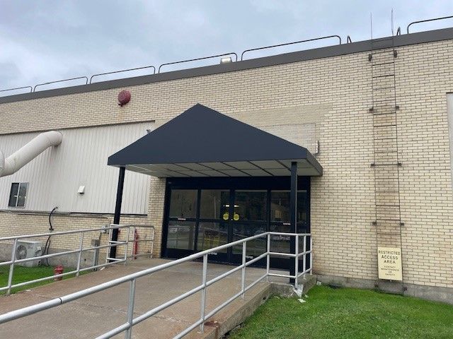 Exterior entrance with a black awning over glass double doors, accessed by a concrete ramp with metal handrails.