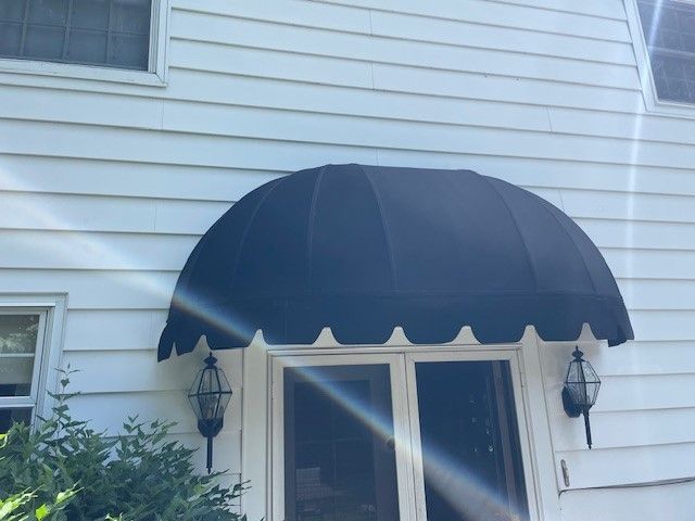 A black rounded fabric awning mounted above a doorway on a white house with horizontal siding.
