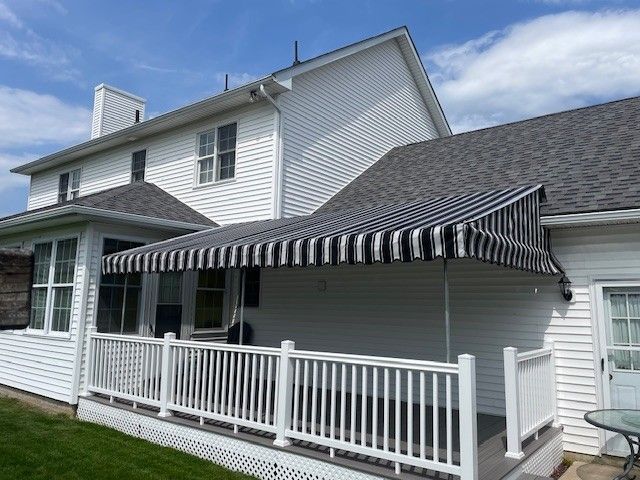 White two-story house with a white deck featuring a black and white striped retractable awning extending over the porch.