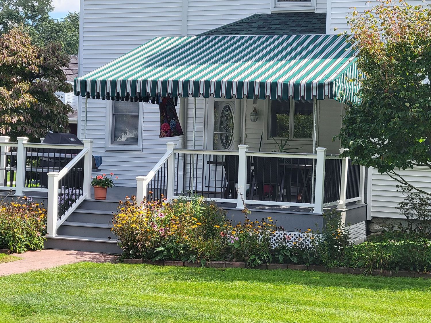 A green-and-white striped awning over a front porch with white railings, stairs, and a small potted flower.