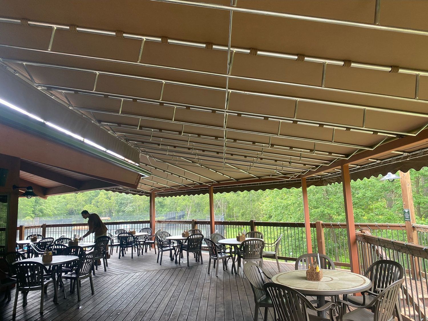 Outdoor deck restaurant with tables, chairs, and a retractable fabric roof overlooking trees.