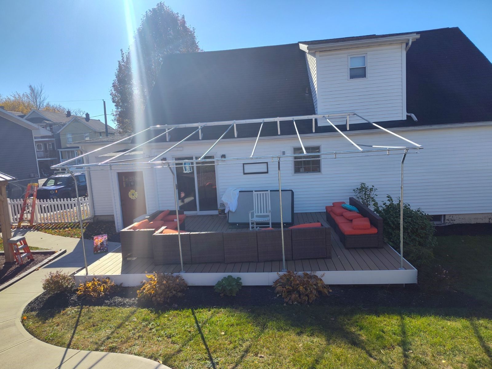 A backyard deck with dark brown wicker sectional furniture, orange cushions, and an unfinished metal pergola frame.