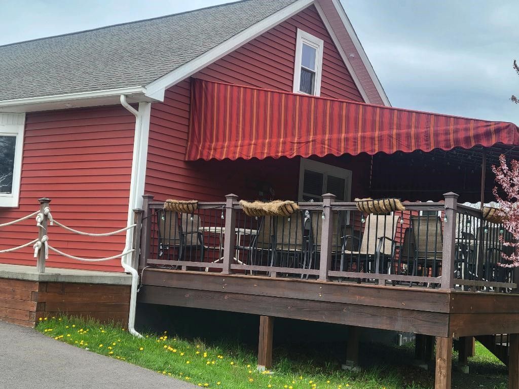A red-sided house with a matching striped awning covering an outdoor wooden deck with seating.