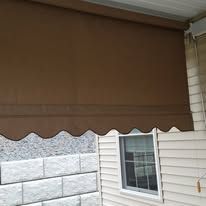 A brown retractable outdoor shade with a scalloped edge mounted on a house exterior above a window.