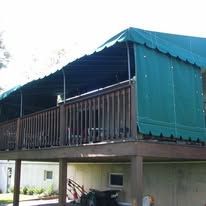 A wooden deck with a green canvas awning cover extending over the railing and side.