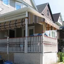 A beige house with a front porch featuring a striped awning, white wooden railings, and lattice skirting.