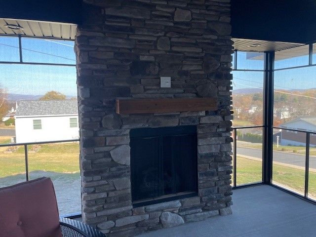 Stone fireplace on a screened porch overlooking a residential area. Brown mantle, dark screen, and gray stone.