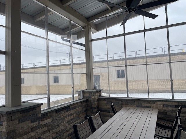 Screened-in porch with a dining table, chairs, and view of a building on a cloudy day.