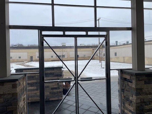 Glass door view to a snow-covered courtyard; buildings, trees, and cloudy sky visible.