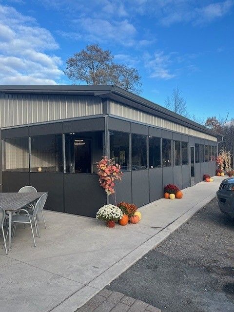 Outdoor dining area with dark gray walls, large windows, pumpkins, and fall flowers, gray patio furniture, and blue sky.