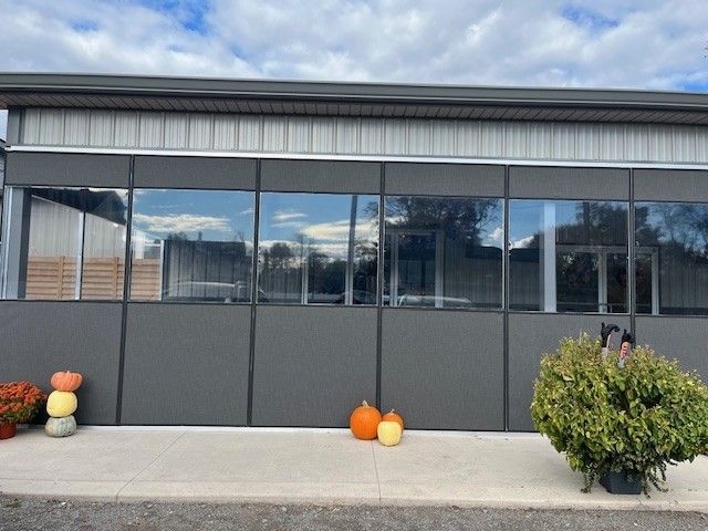 Exterior of a modern grey building with large windows, decorated with pumpkins and a green bush on a concrete walkway.