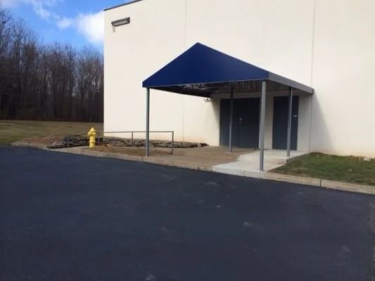 Exterior building entrance with blue awning, concrete ramp, and fire hydrant.