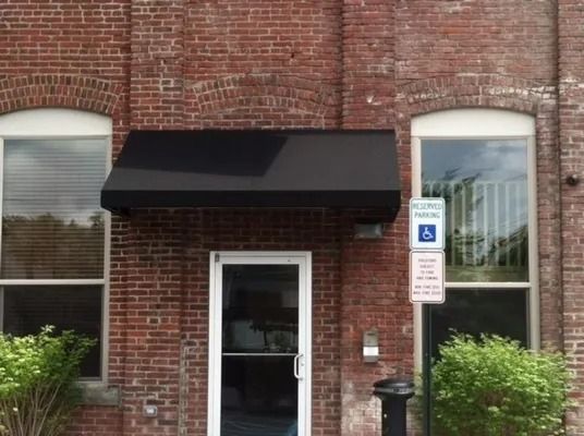Brick building entrance with black awning, glass door, two windows, and accessible parking sign.