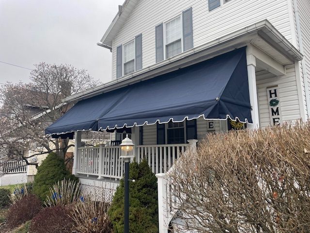 A white house with a porch, featuring a large dark blue retractable awning above the entrance.