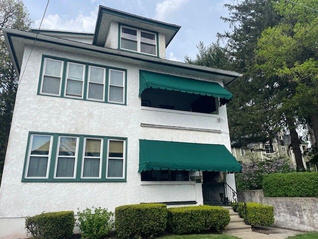 A two-story white stucco building with a green roof, green-trimmed windows, and green awnings over the entry and porch.
