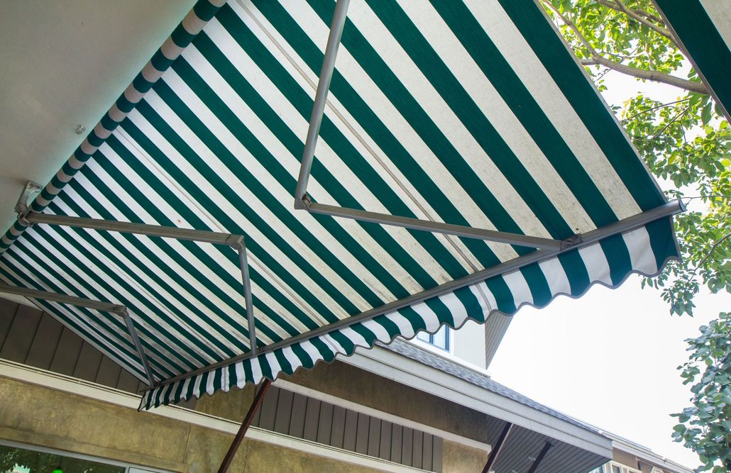 A retractable awning with white and forest-green vertical stripes mounted above an exterior wall.