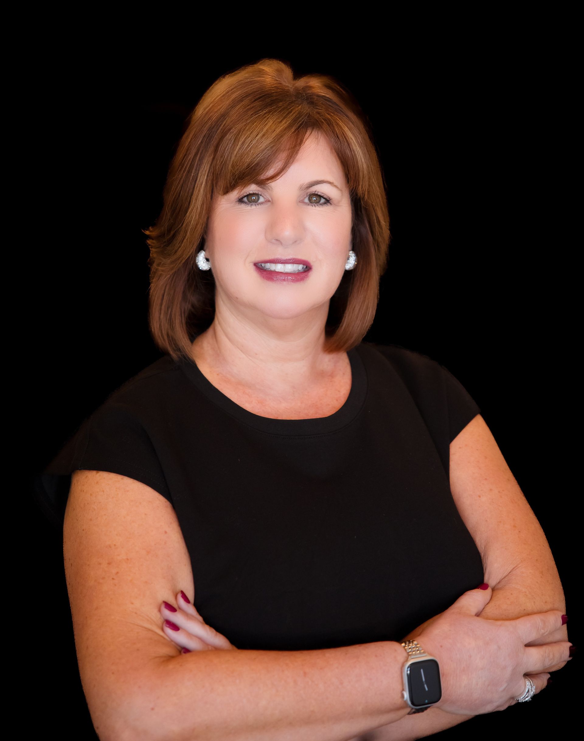 Portrait of a smiling woman in a black top with folded arms against a black background