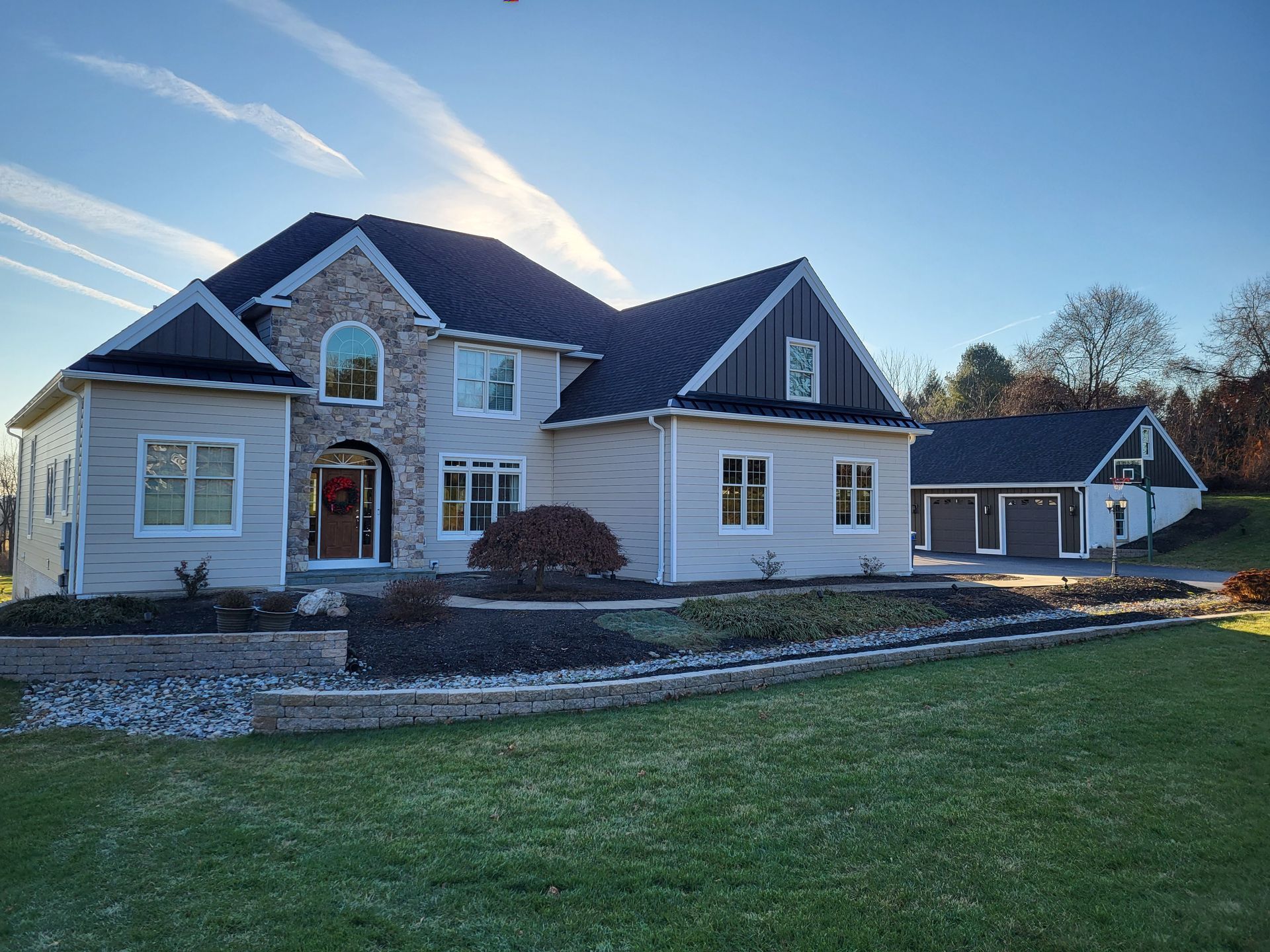 Large two-story house with stone accents and a detached garage on a sunny day; green lawn and blue sky.