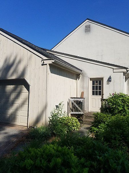 Beige building exterior with a garage, door, and overgrown shrubs.