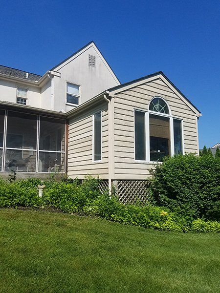 Beige house addition with arched window, attached to a two-story white house, lush green lawn and blue sky.