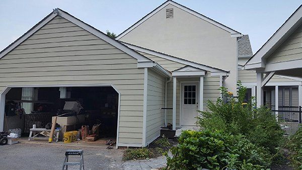 Garage and house exterior with light siding and white trim, a door, and greenery.