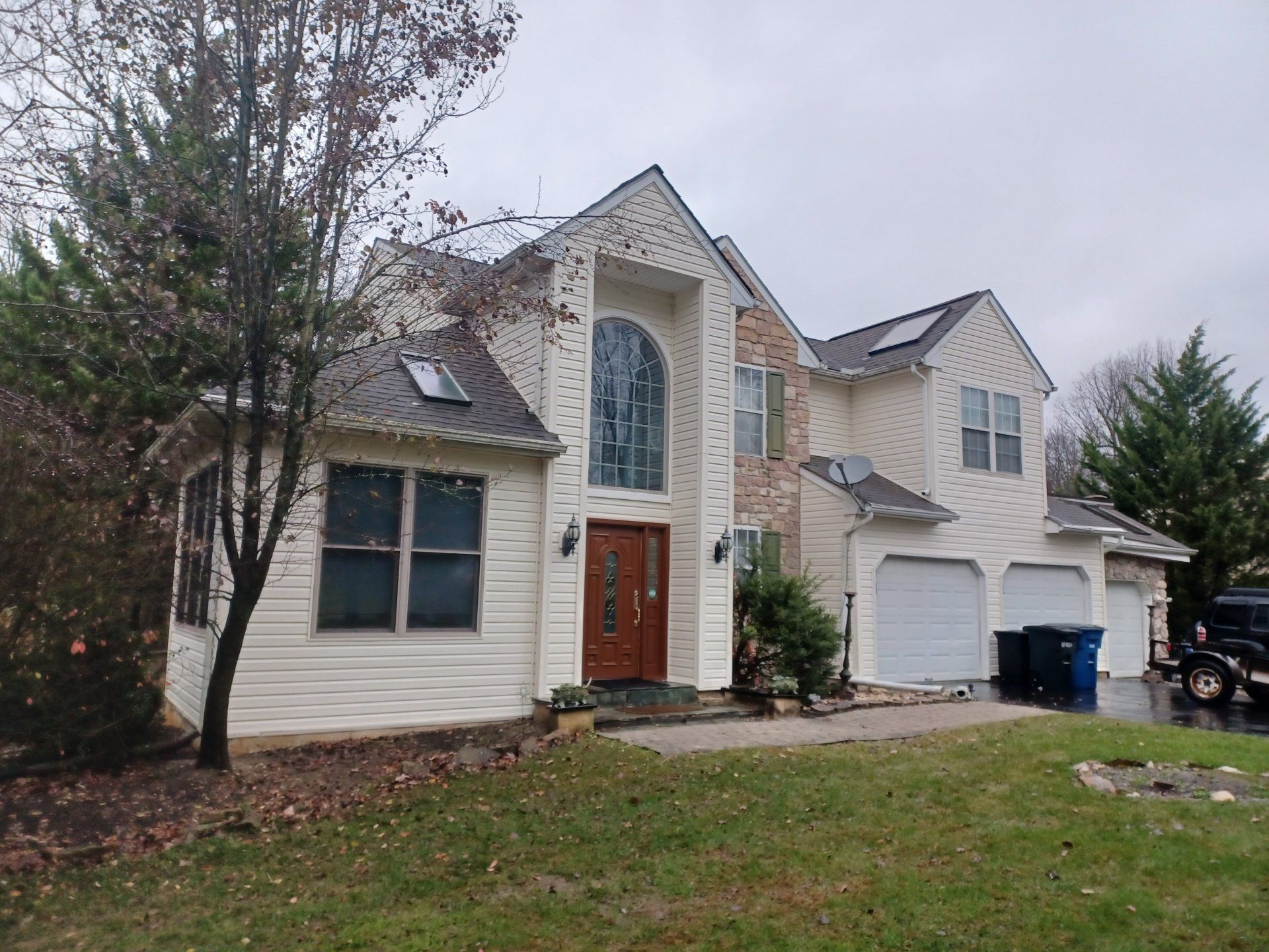 Two-story house with beige siding, brown door, three-car garage, and green lawn. Overcast day.