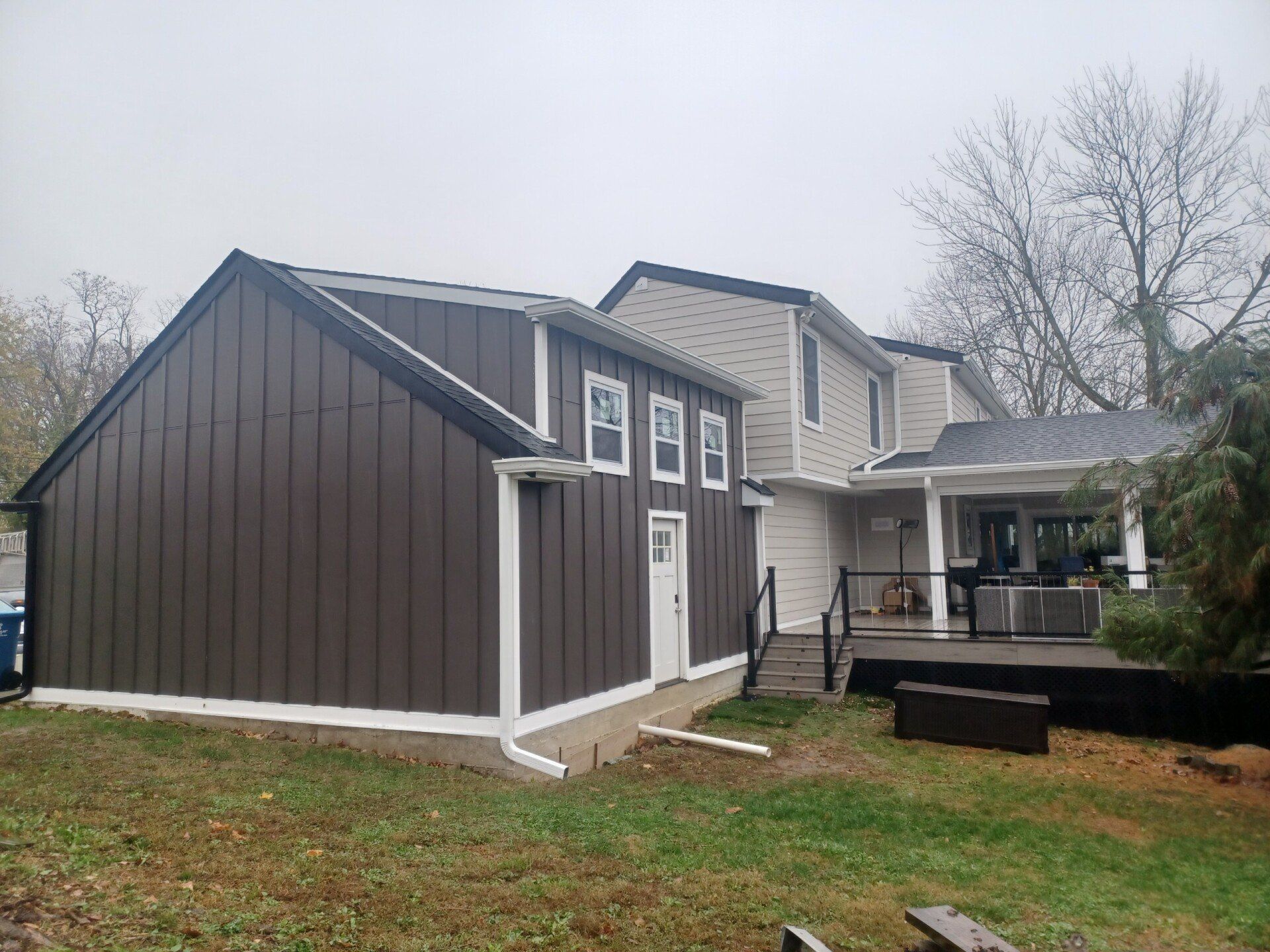 Brown and beige house with attached shed, windows, and a back deck on an overcast day.