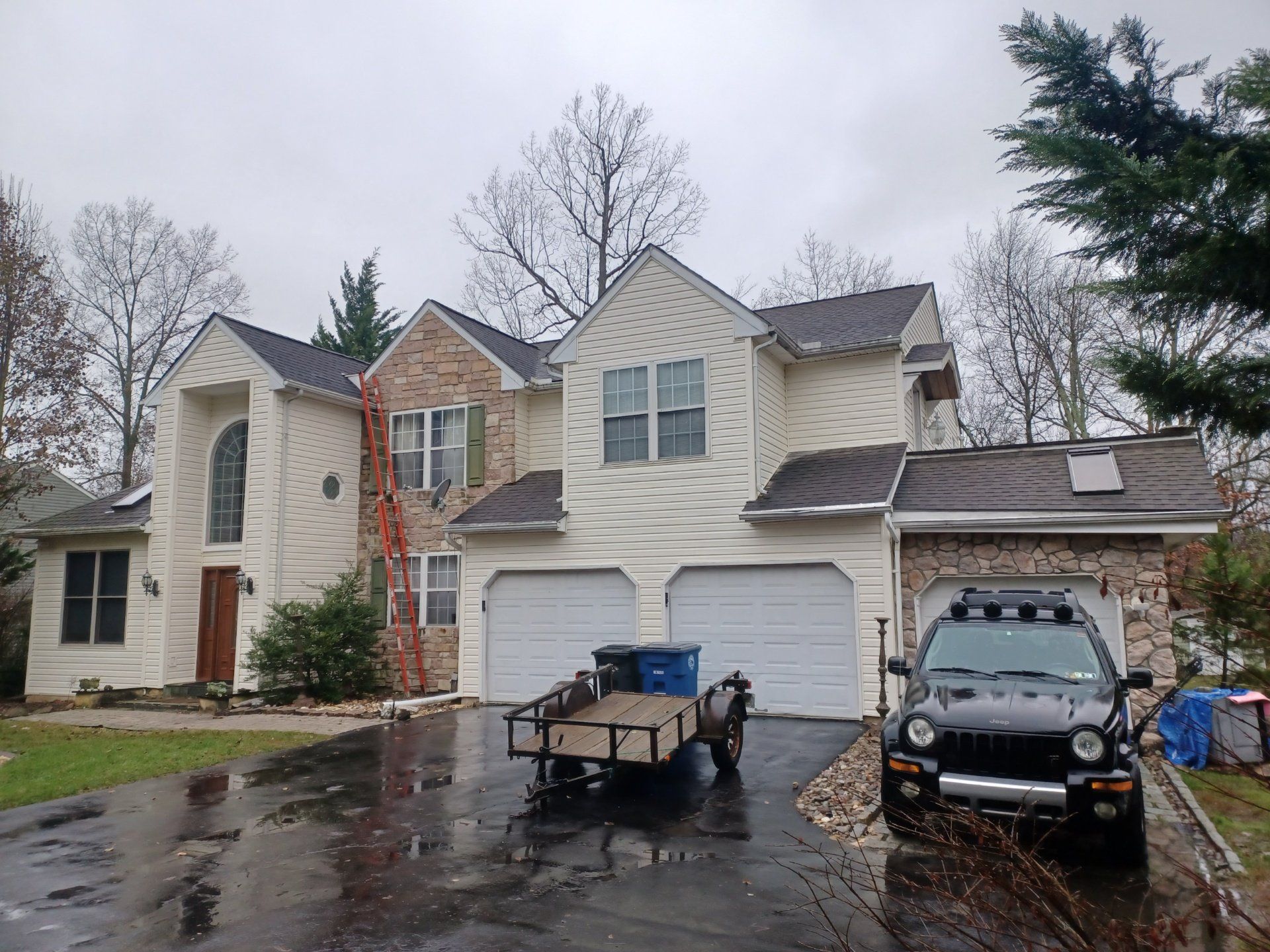 Two-story house with beige siding, brown roof, brick accents, and a black vehicle parked in the driveway.