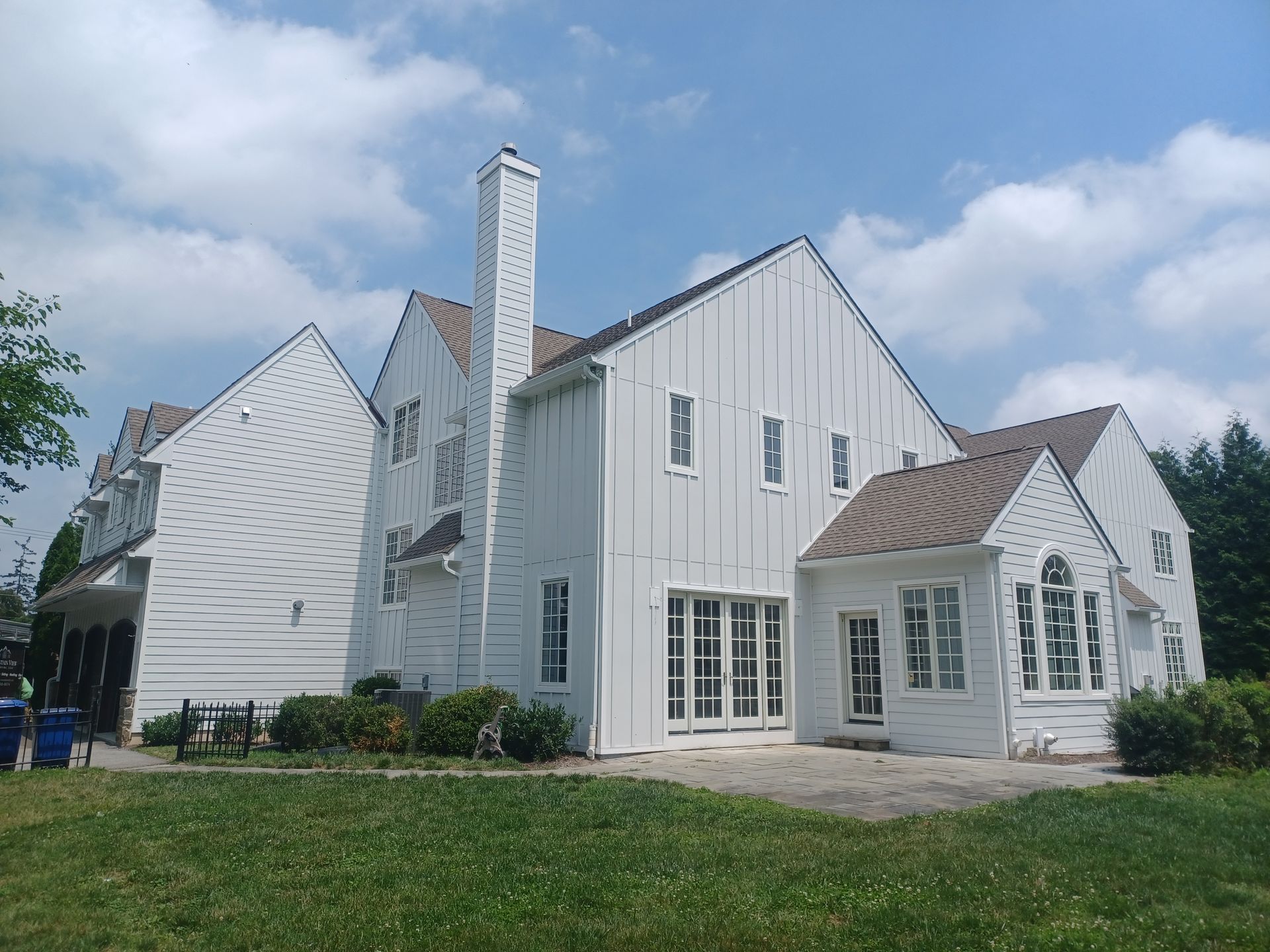 White house with multiple gabled sections and a tall chimney against a cloudy sky, seen from a grassy yard.