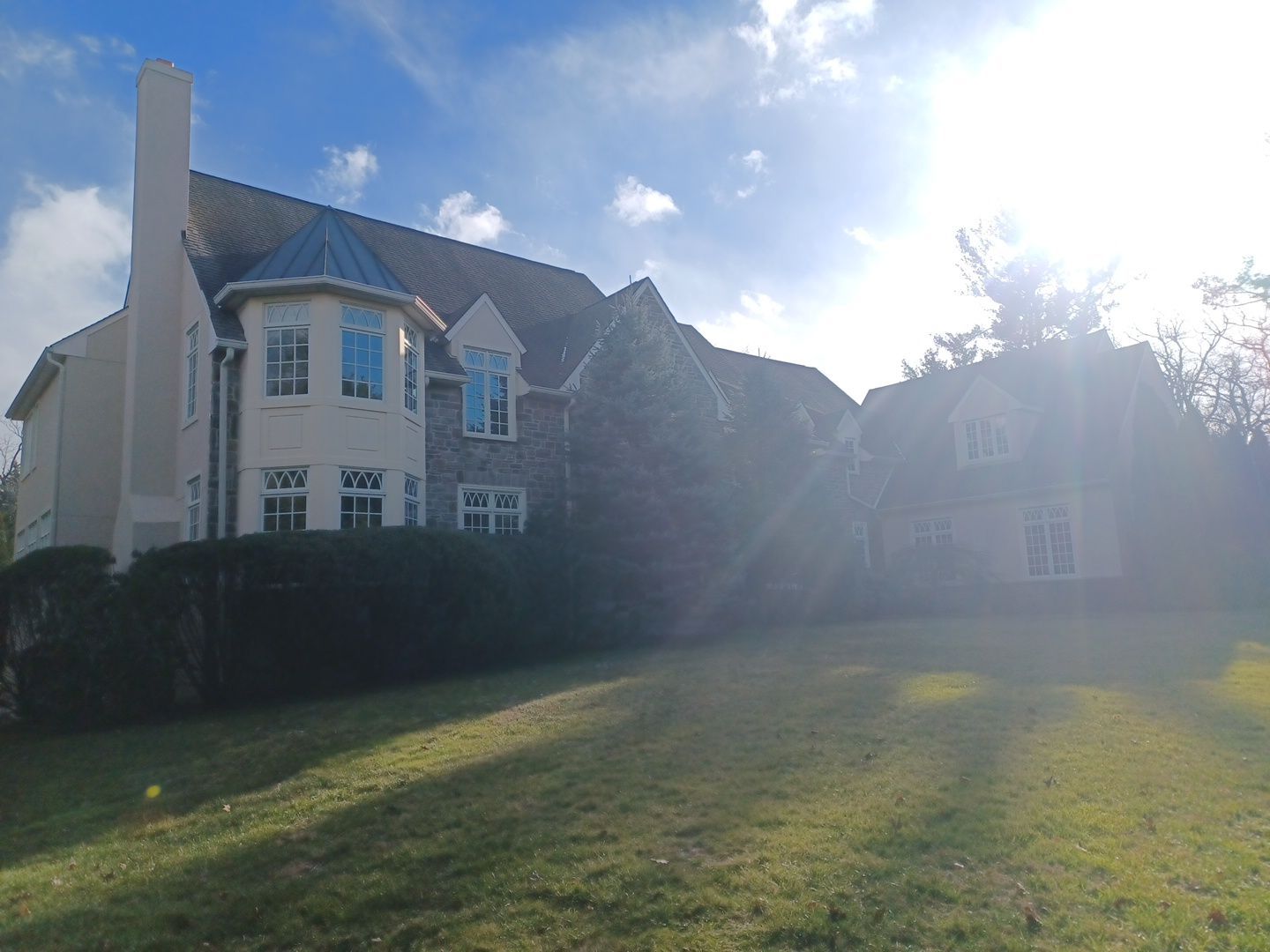 Large house with a stone and beige facade, set in a grassy yard on a sunny day.