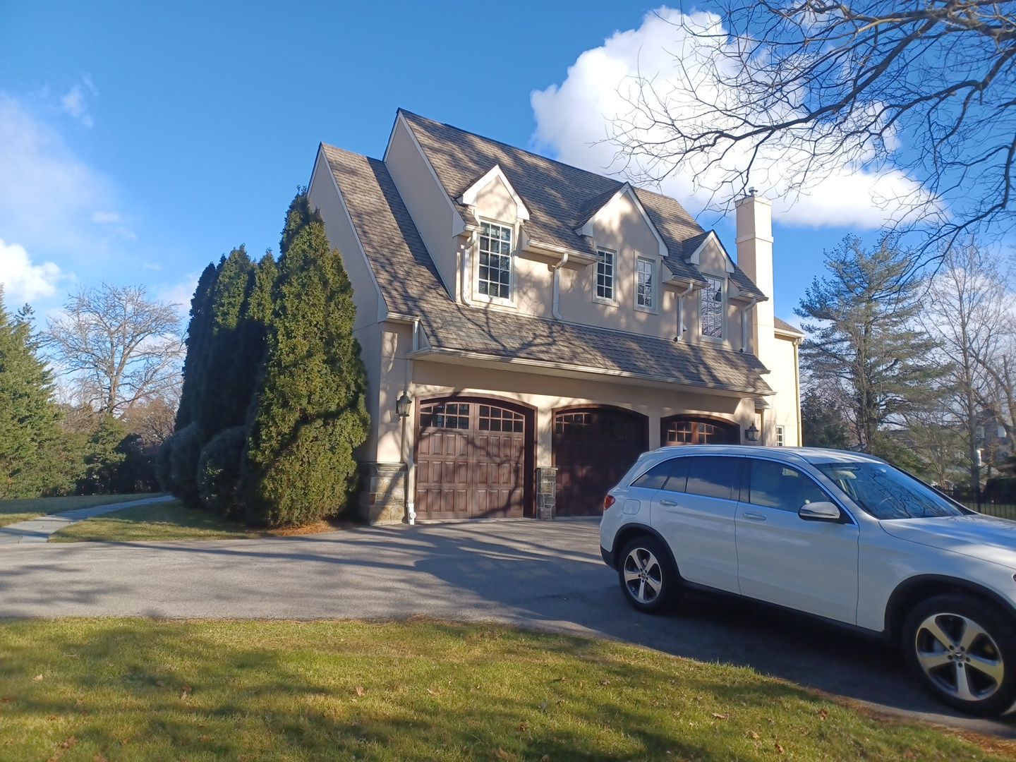 House with brown garage doors, white SUV parked in the driveway, green lawn, and blue sky with some clouds.