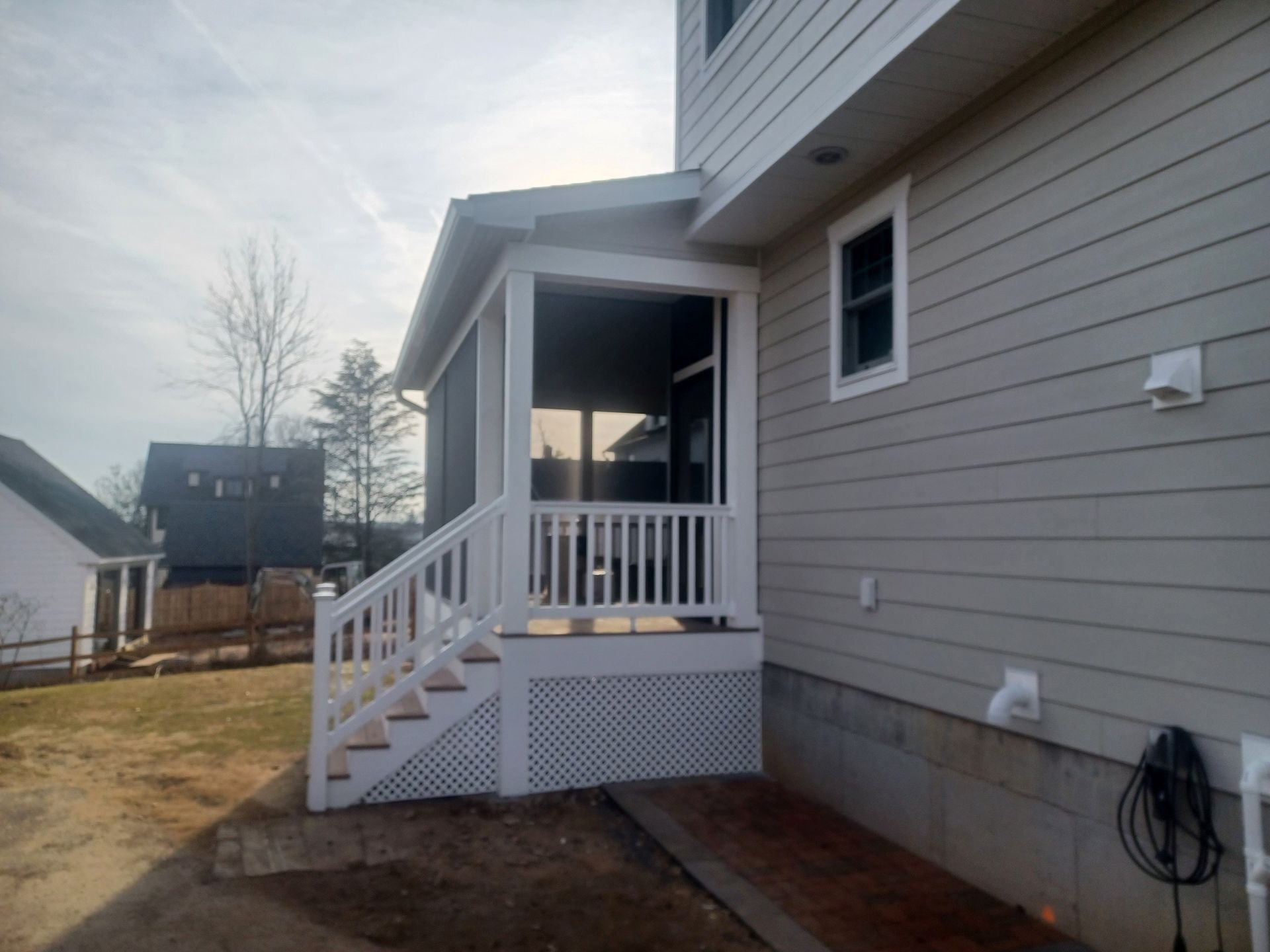 White screened porch with stairs and railing attached to a beige house, overcast sky.