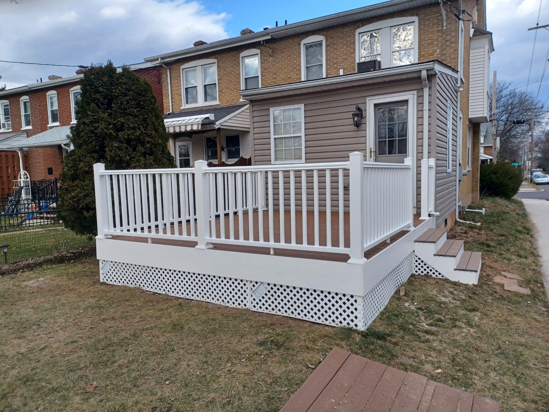 White-railed deck attached to a brown-sided building, overlooking a yard with patchy grass.