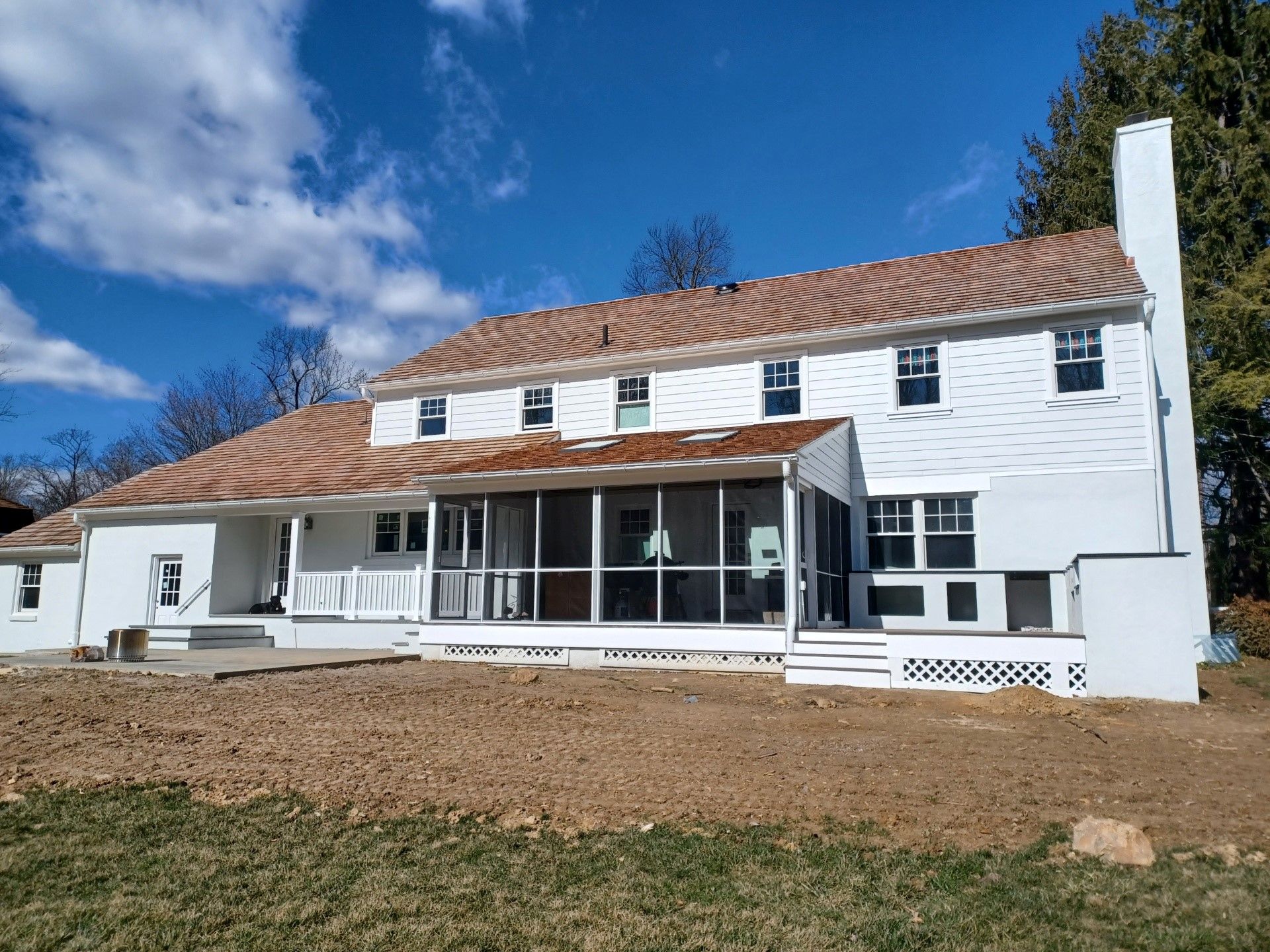 White two-story house with brown roof, screened-in porch, and chimney, set against a blue sky.