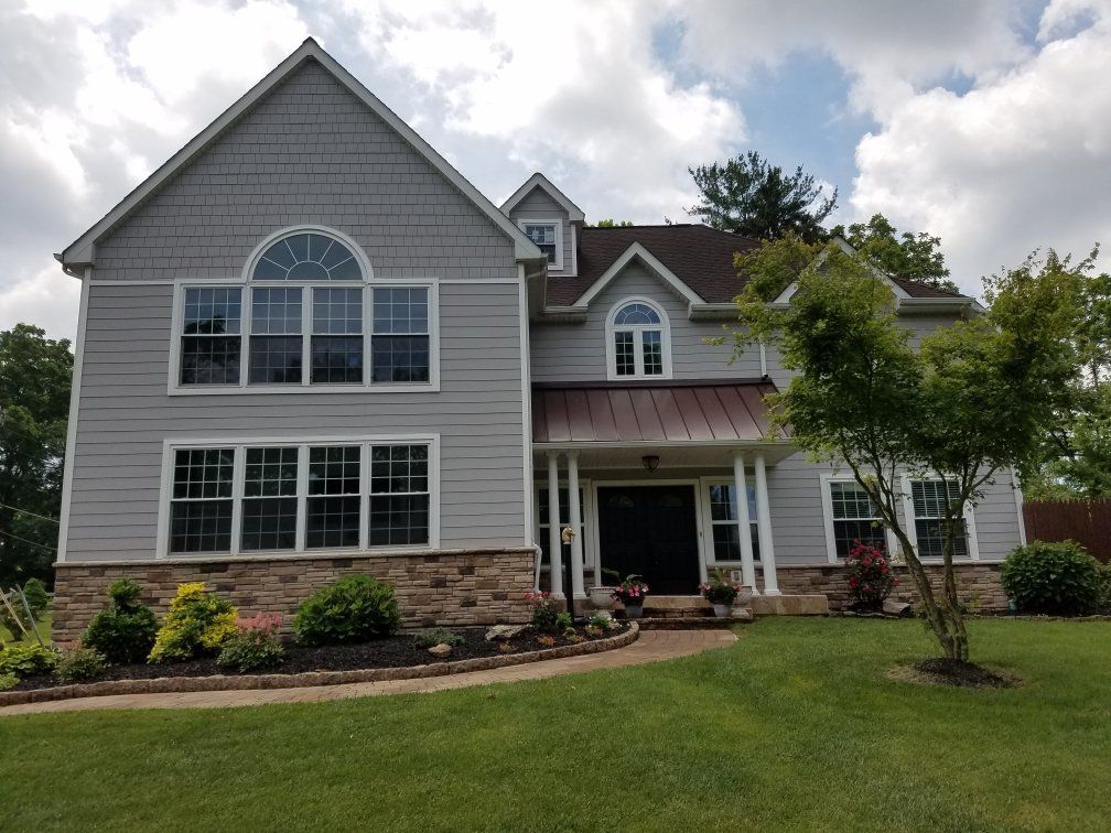 Two-story gray house with stone accents, manicured lawn, and a small tree.