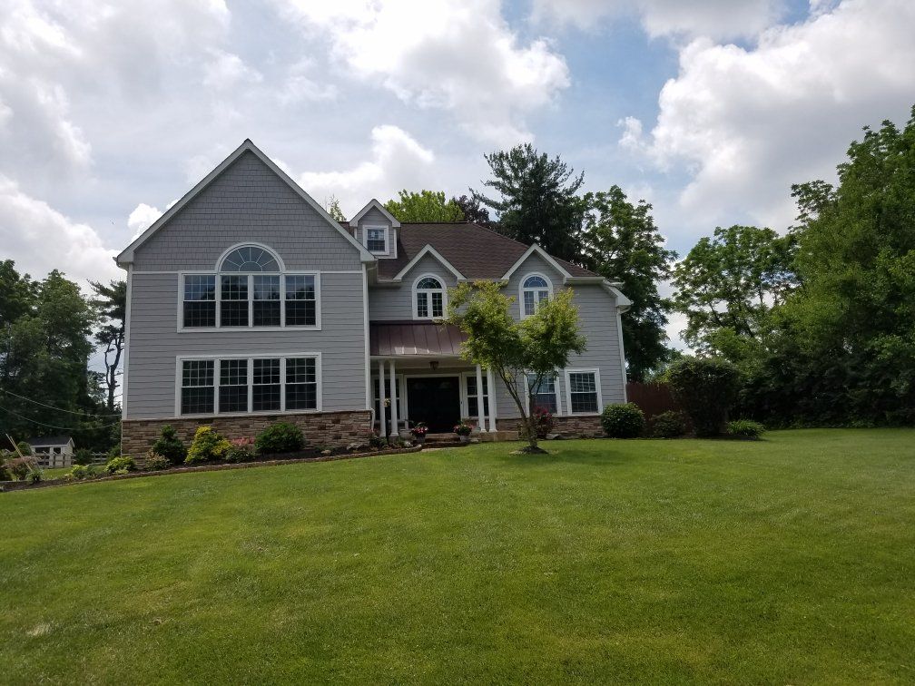 Gray two-story house with large windows, green lawn, blue sky with clouds.