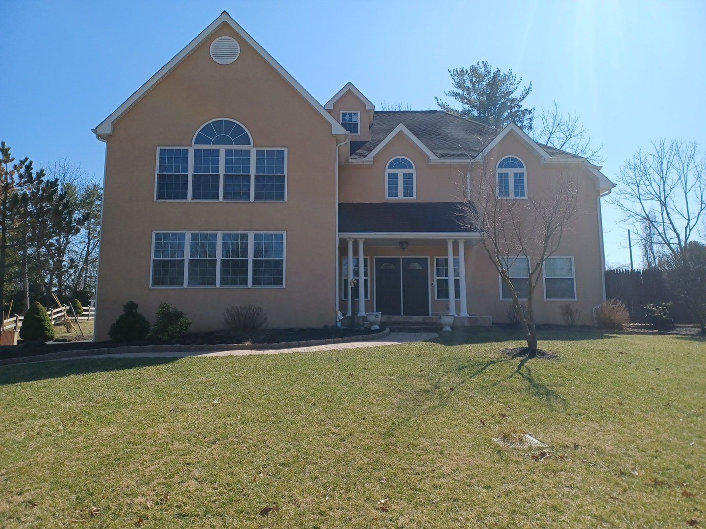 Two-story beige house with large windows on a sunny day, green lawn in the front.