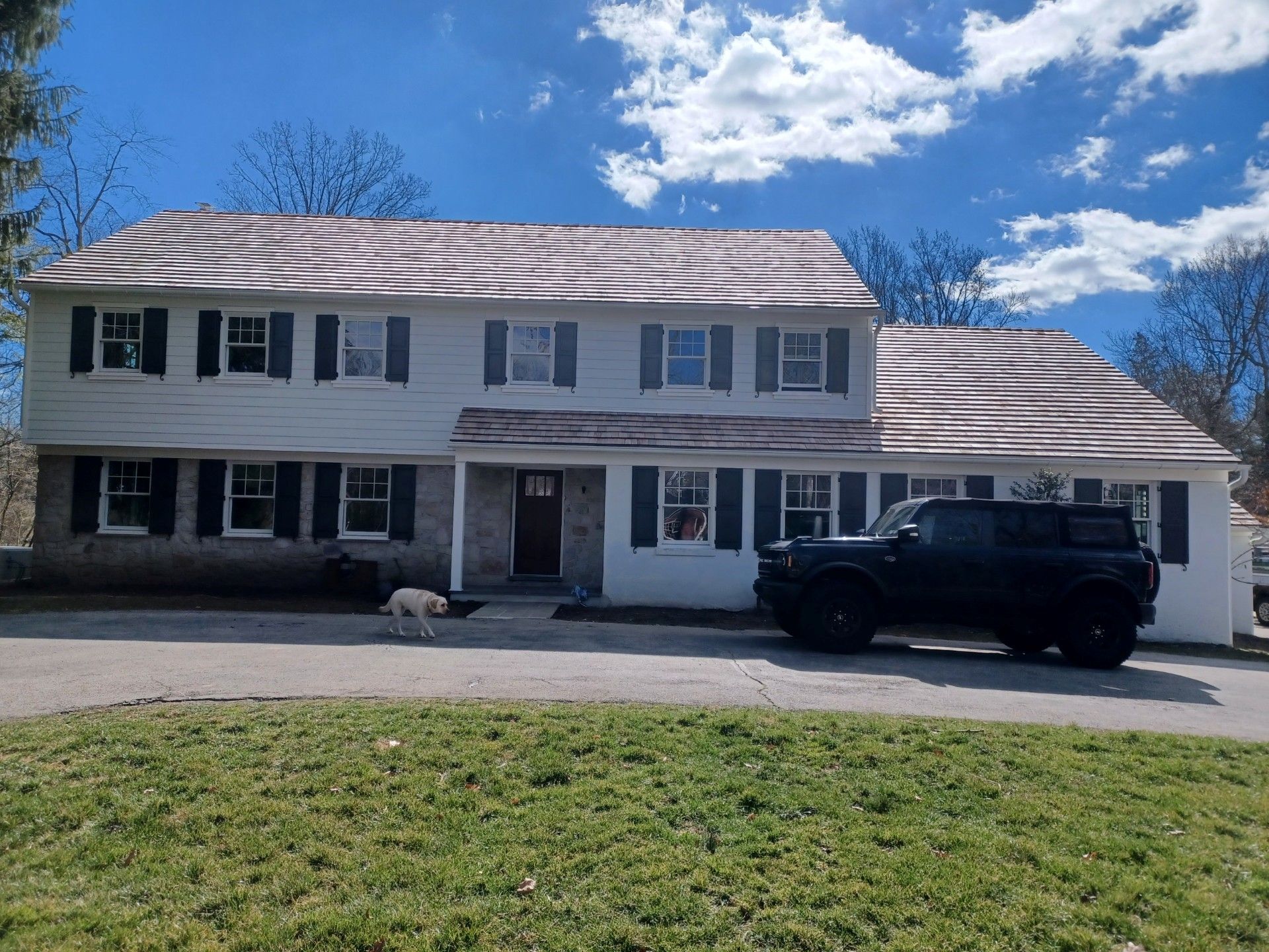 Two-story white house with black shutters, gray stone siding, and a dark SUV parked in front.