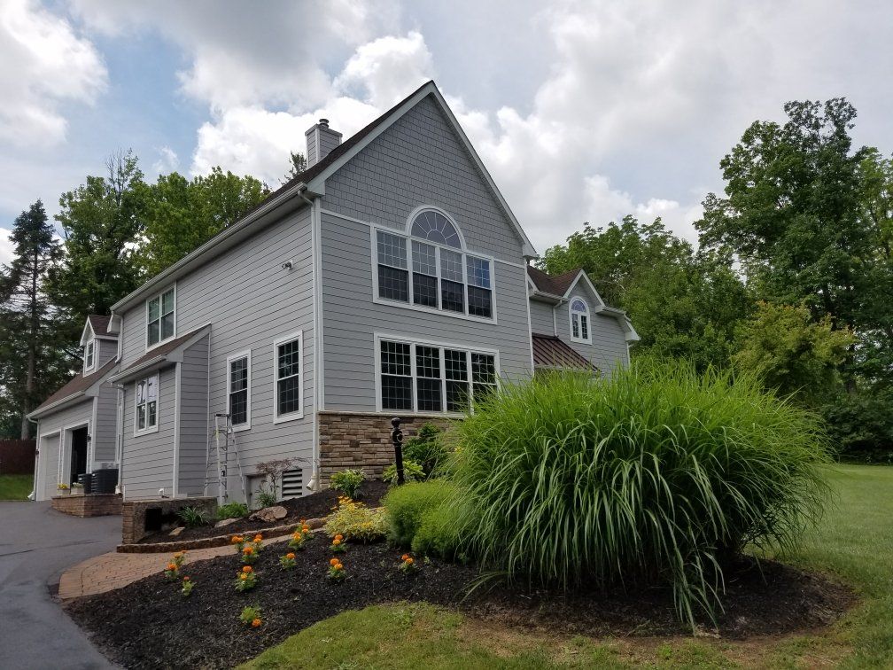 Two-story gray house with manicured lawn and landscaping under a cloudy sky.