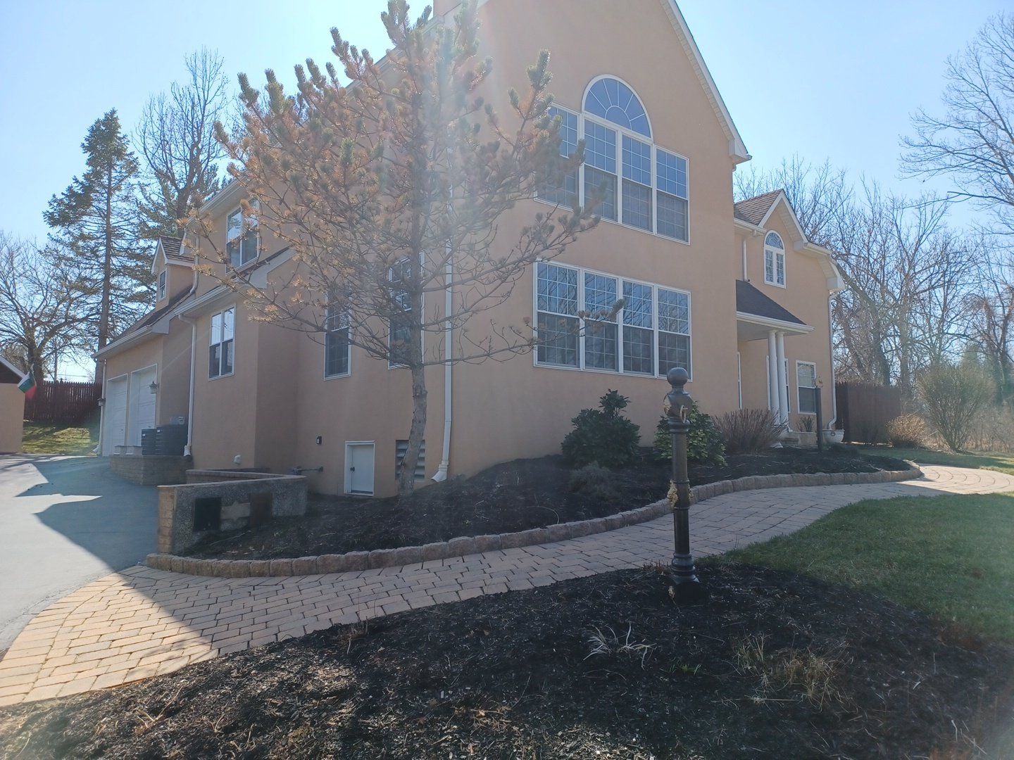 Beige stucco house with a curving brick path and landscaping on a sunny day.