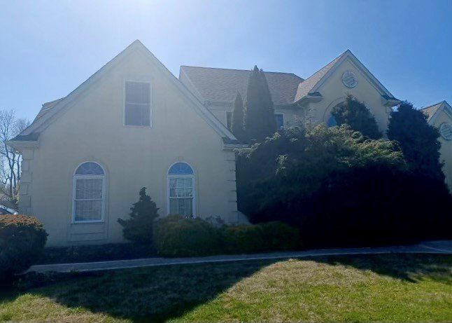 Light yellow house with arched windows and tall, dark green bushes in front. Sunny day.