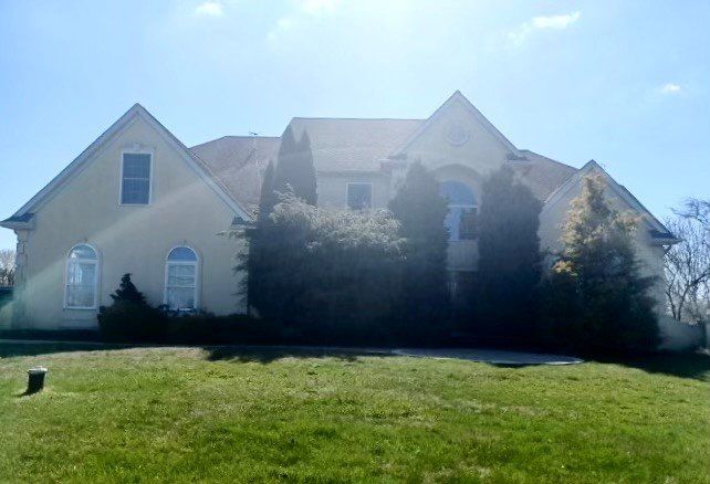 Large beige house with a grassy front lawn under a bright blue sky.